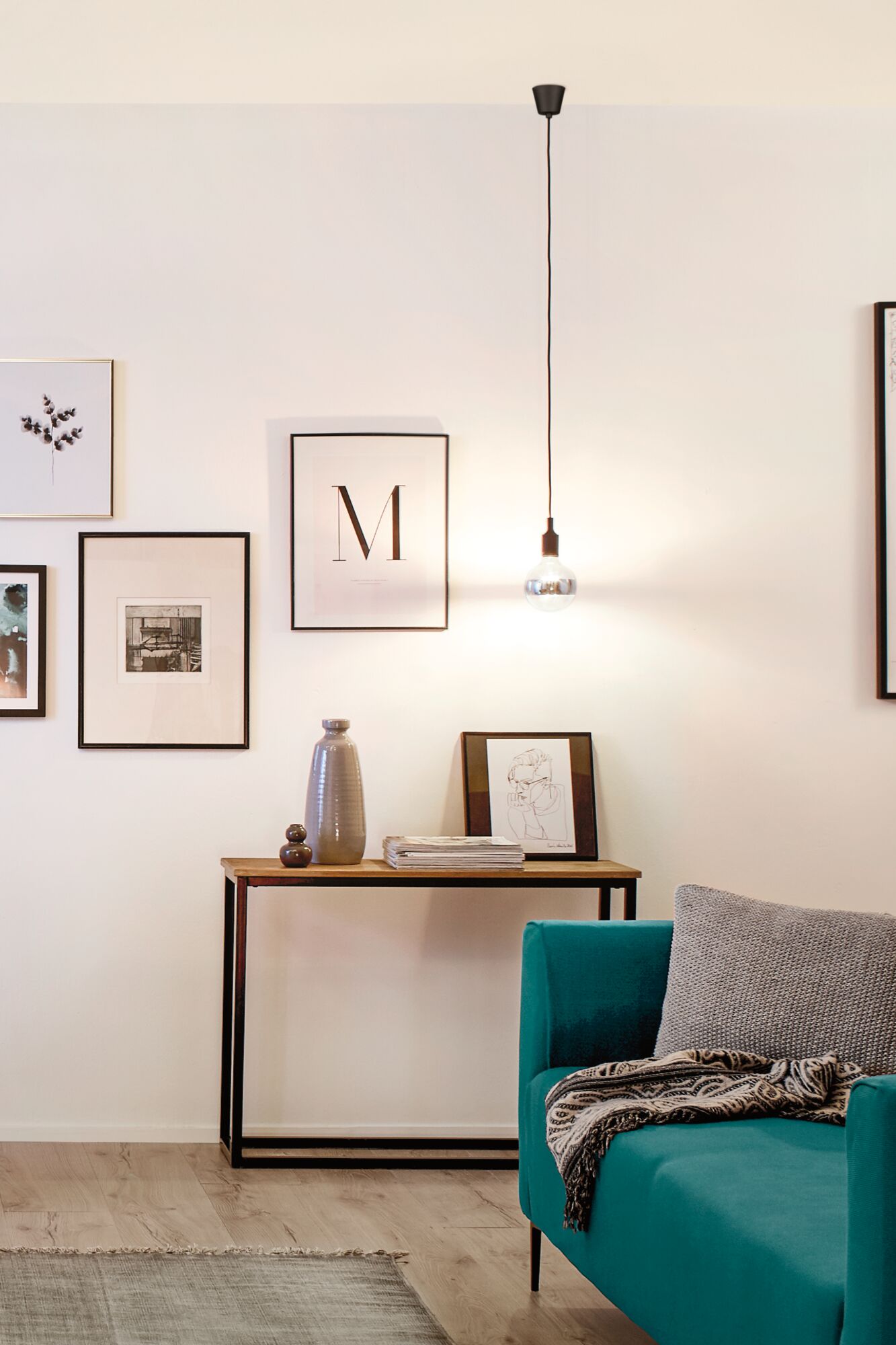 Salon moderne avec console en métal noir, plateau en bois, vase gris et canapé turquoise avec coussin et plaid