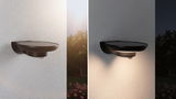 Black metal LED outdoor wall light with motion sensor shown in day and night garden setting