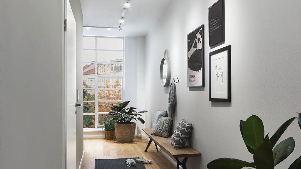 Moderne gang met houten bank, planten en witte NanoRail spots aan het plafond voor helder licht.