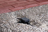 Black plastic junction box with cables on gravel near red paving for outdoor lighting setup