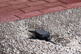 Black plastic junction box with cables in gravel bed next to red paving for outdoor lighting setup