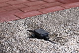 Black plastic junction box with cables in gravel bed next to red paving for outdoor lighting setup