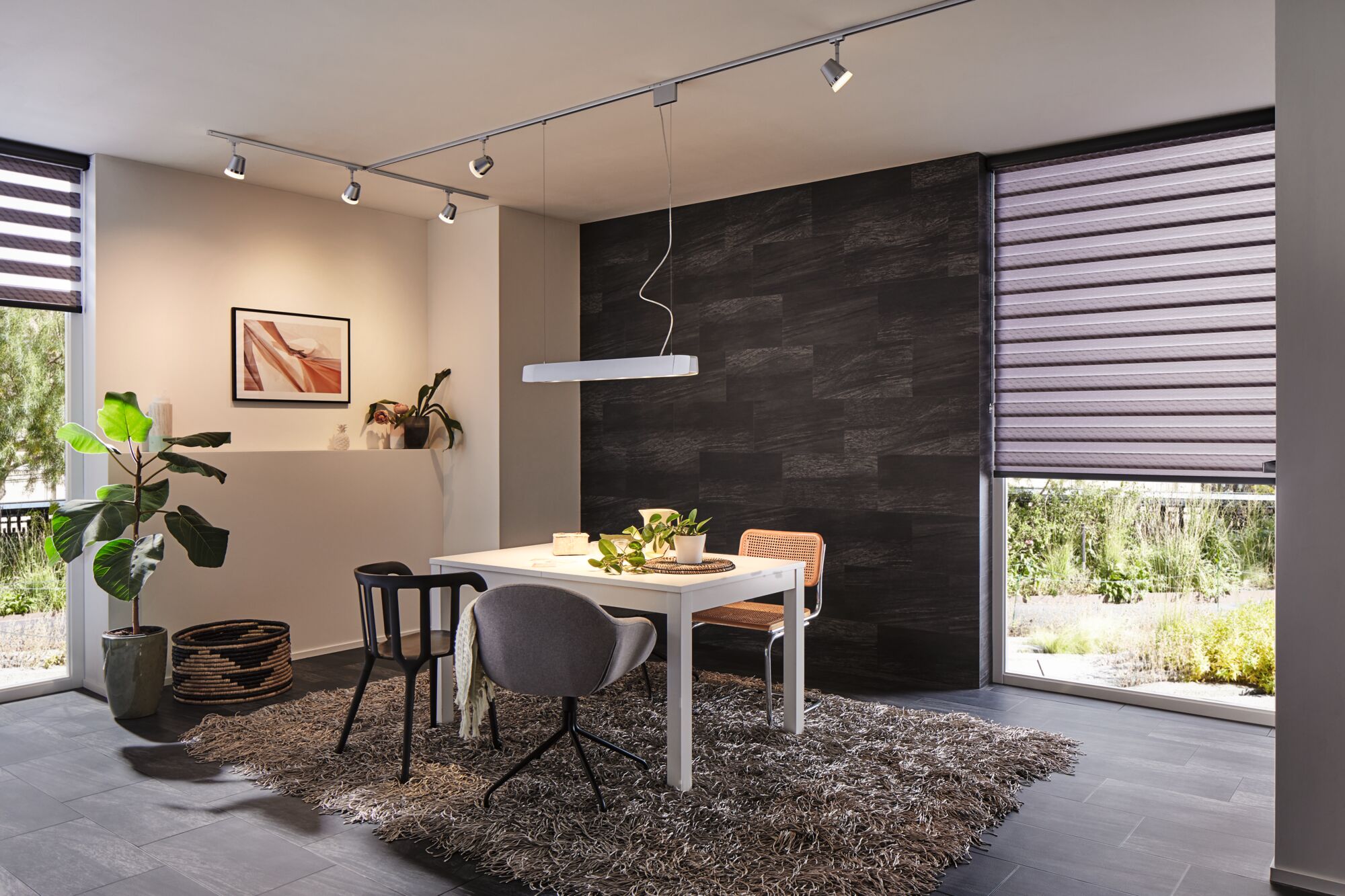 Moderne spisestue med hvidt bord, blandede stole, gråt tæppe, oplyst af Paulmann LED-spotlights og pendel.