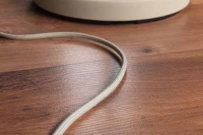 Close-up of grey fabric cable on brown wooden floor with partial view of white object