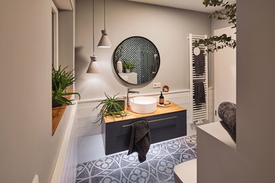Modern bathroom with dark grey floating vanity, wooden countertop, round mirror, plants, and pendant lights