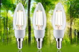 Three clear glass LED candle bulbs with E14 base shown against a green forest background